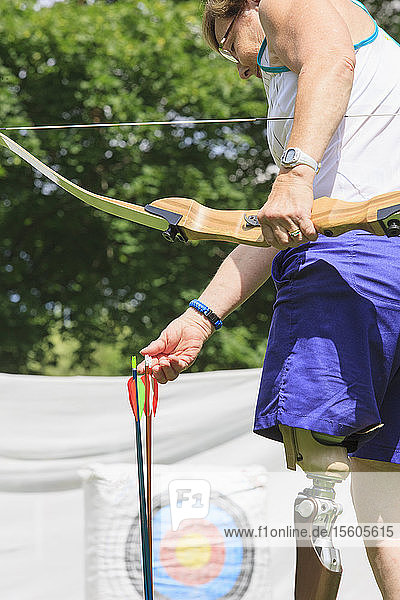 Woman with prosthetic leg preparing for archery practice with bow and arrows
