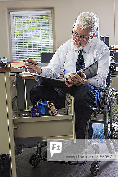 Mann mit Muskeldystrophie im Rollstuhl schaut auf eine Akte in seiner Schreibtischschublade