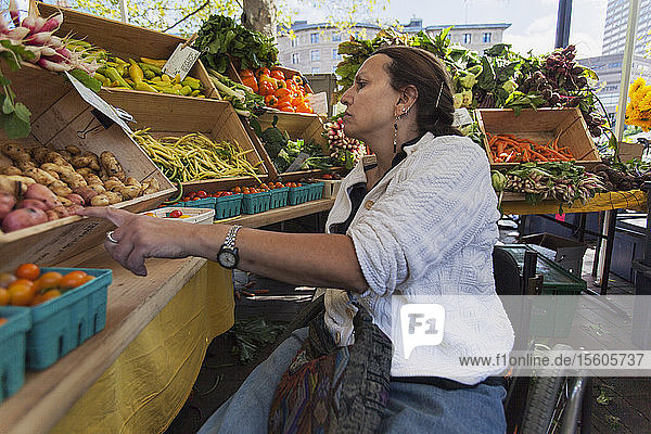 Frau mit Rückenmarksverletzung im Rollstuhl beim Einkaufen auf dem Wochenmarkt