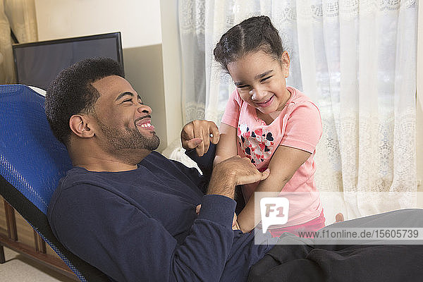 African American man with Cerebral Palsy having fun with his daughter at home