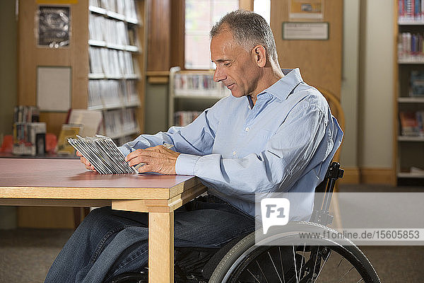 Mann mit Rückenmarksverletzung in einer Bibliothek  der sich DVDs ansieht
