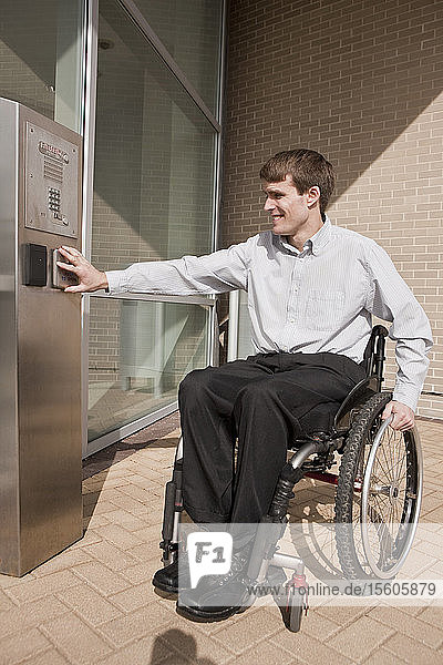 Businessman with spinal cord injury in a wheelchair pushing a button to open a door