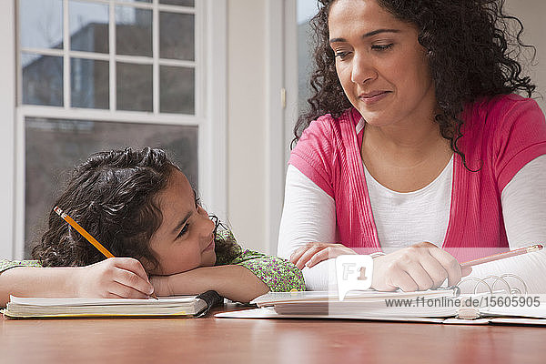 Hispanische Frau  die ihrer Tochter bei den Hausaufgaben hilft