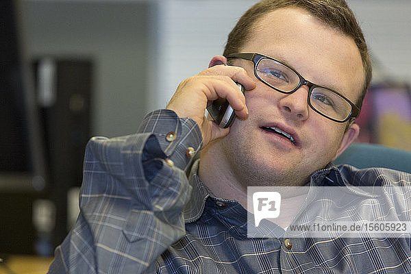 Hospital aid worker with Down Syndrome sitting at his desk and using his cell phone in office