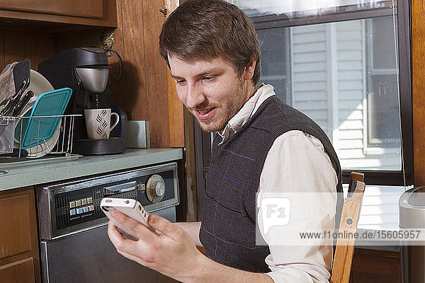 Blinder Mann in seiner Küche  der Hilfsmittel auf seinem Mobiltelefon hört
