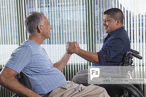 Zwei Männer mit Rückenmarksverletzungen beim Händeschütteln in einem Büro