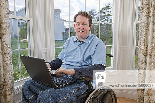 Geschäftsmann mit Querschnittslähmung im Rollstuhl  der mit behinderten Händen an einem Laptop arbeitet