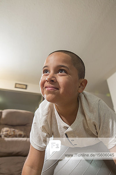 Glücklicher hispanischer Junge mit Autismus  der mit einem Übungsball im Wohnzimmer spielt