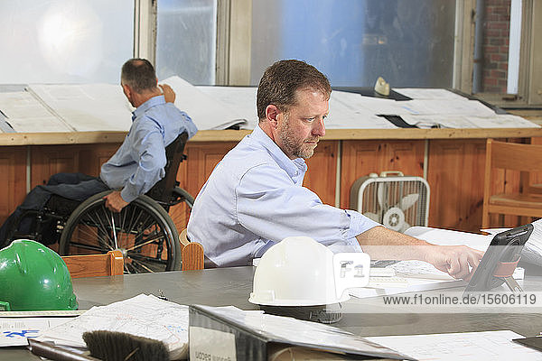 Zwei Projektingenieure  einer mit einer Rückenmarksverletzung im Rollstuhl  arbeiten im Büro