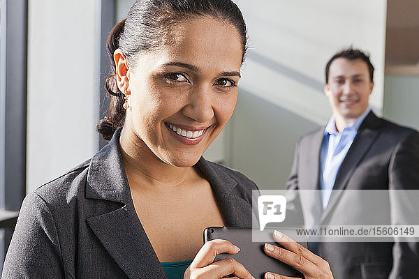 Businesswoman holding tablet with businessman behind her