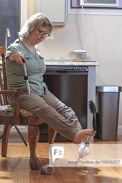 Frau mit TAR-Syndrom  die ihre Haarbürste mit den Füßen aufhebt