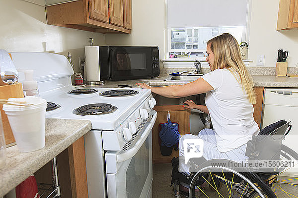 Frau mit Querschnittslähmung bereitet in ihrer barrierefreien Küche Essen zu