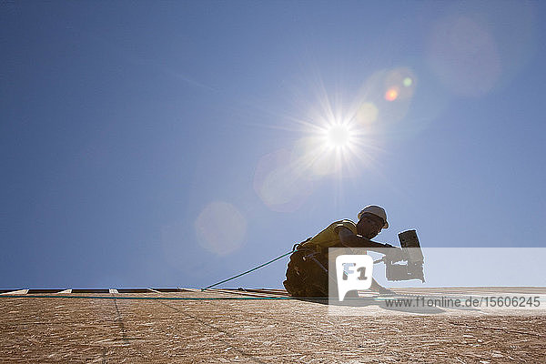 Ein spanischer Zimmermann benutzt eine Nagelpistole auf dem Dach eines im Bau befindlichen Hauses