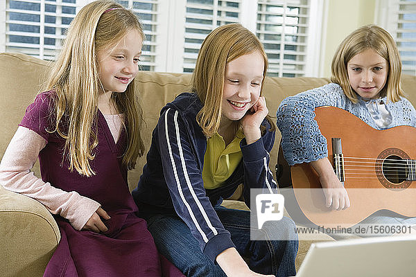 Blick auf drei Mädchen  die einen Laptop bedienen.