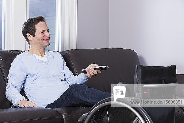 Man with spinal cord injury with leg in wheelchair watching TV with remote
