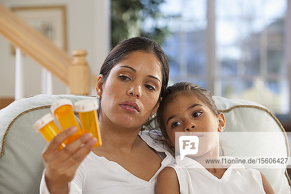 Hispanische Frau sitzt mit ihrer Tochter und hält Pillenflaschen