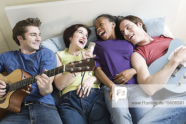 Zwei Männer und eine Frau liegen mit Gitarren und Mikrofon auf einem Bett.