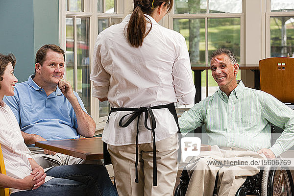 Zwei Männer im Rollstuhl mit Rückenmarksverletzungen und ein Freund bestellen Essen in einem Café.