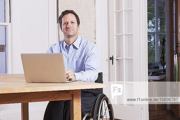 Man with spinal cord injury sitting in a wheelchair working on laptop