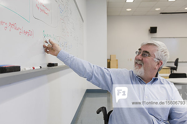 Universitätsprofessor mit Muskeldystrophie schreibt auf einer Tafel in einem Klassenzimmer