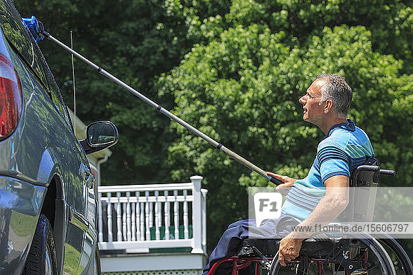 Man with a Spinal Cord Injury in wheelchair washing his accessible car