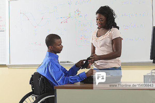 Zwei Ingenieurstudenten  einer im Rollstuhl  betrachten ein elektronisches Tablet in einem Klassenzimmer