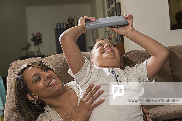 Hispanischer Junge mit Autismus spielt mit seiner Mutter zu Hause ein elektronisches Spiel