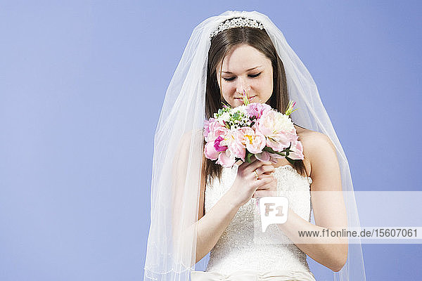 Junge Frau im Hochzeitskleid hält Blumen.