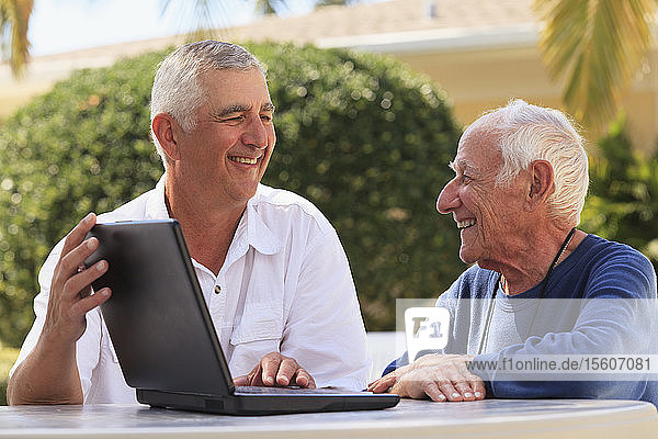 Ein älterer Mann zeigt seinem sehbehinderten Vater lächelnd einen Laptop