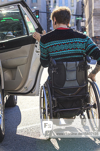 Trendiger Mann mit einer Rückenmarksverletzung im Rollstuhl steigt in ein Taxi ein