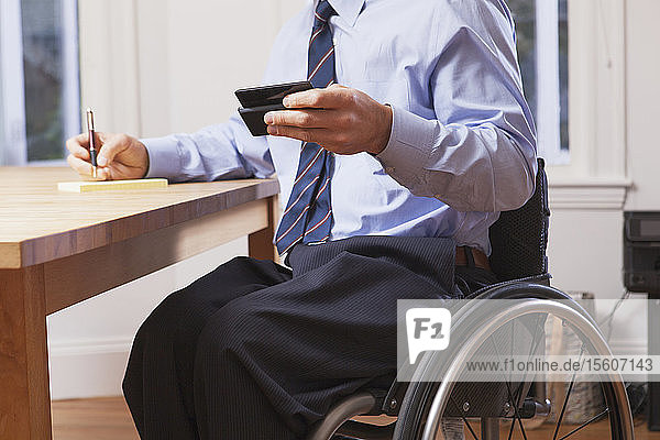 Geschäftsmann mit Querschnittslähmung im Rollstuhl  der ein Smartphone benutzt