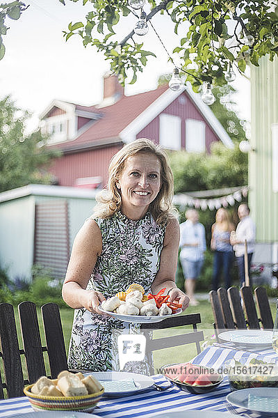 Porträt einer lächelnden  reifen Frau  die im Hinterhof einen Speiseteller am Tisch hält