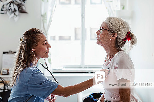Seitenansicht einer Ärztin  die einen älteren Patienten in einer medizinischen Klinik untersucht