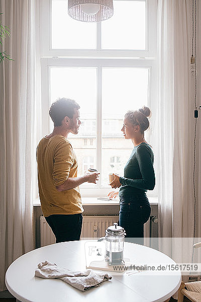 Seitenansicht eines Paares  das sich unterhält  während es zu Hause am Fenster steht