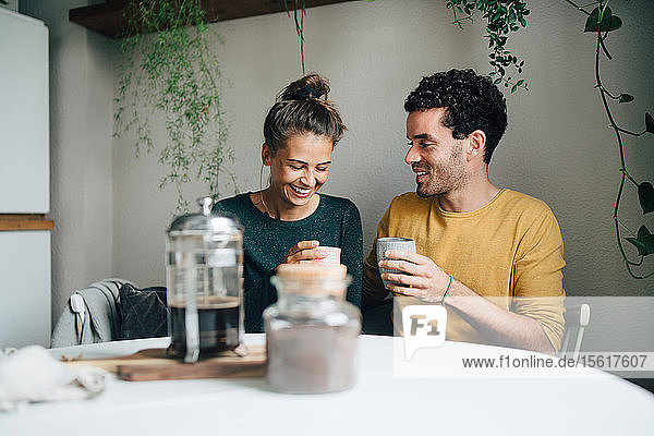 Lächelnder Freund und Freundin beim Kaffeetrinken am Wohnzimmertisch