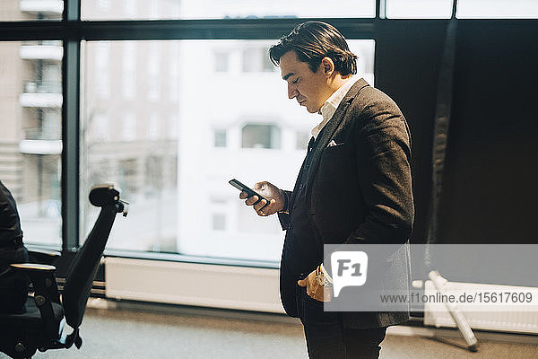 Side view of businessman using mobile phone while standing at workplace