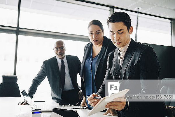 Young businessman discussing with colleagues over digital tablet in conference room at office