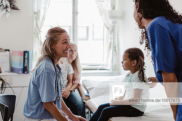 Fröhliche Kinderärztin im Gespräch mit Krankenschwester bei Untersuchung eines Mädchens in medizinischer Klinik