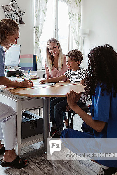 Arzt betrachtet Patient  der auf Papier zeigt  während Krankenschwester und Mutter im Krankenhaus am Schreibtisch sitzen