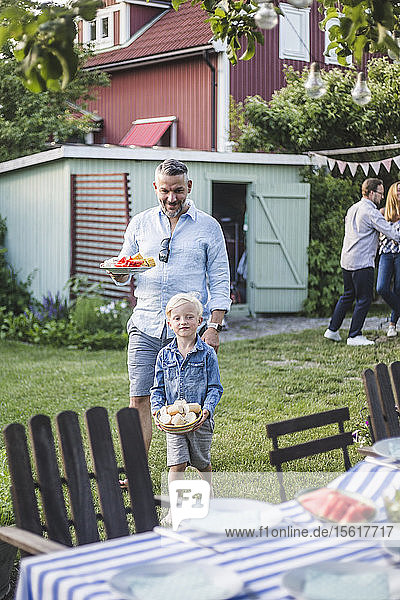 Vater und Sohn gehen am Wochenende mit einem Teller zum Esstisch für eine Gartenparty im Garten