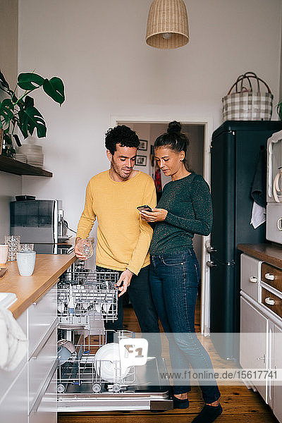 Woman showing mobile phone to boyfriend while standing in kitchen