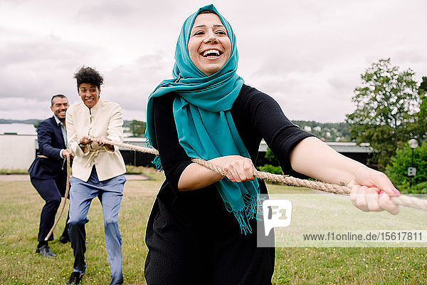 Lächelnde multiethnische männliche und weibliche Kollegen ziehen am Seil und spielen Tauziehen auf dem Rasen