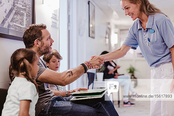 Lächelnde Ärztin begrüsst Mann  der mit Sohn und Tochter im Krankenhauskorridor wartet