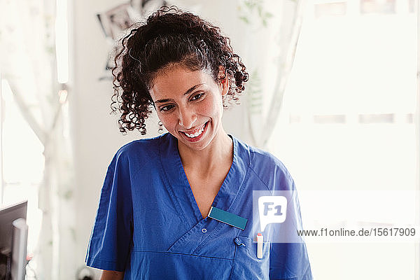 Lächelnde Krankenschwester mit lockigem Haar schaut im Krankenhaus weg