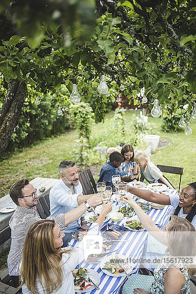 Schrägansicht von Freunden  die während einer Gartenparty im Sommer auf Weingläser anstoßen