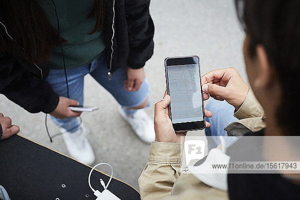 Hochwinkelansicht eines Mannes  der im Stehen mit Freunden die Karte auf einem Smartphone überprüft