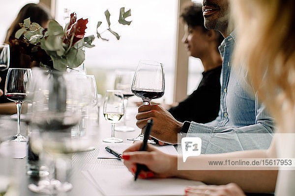 Geschäftsmann hält Weinglas in der Hand  während er mit Kollegen am Tisch im Kongresszentrum sitzt