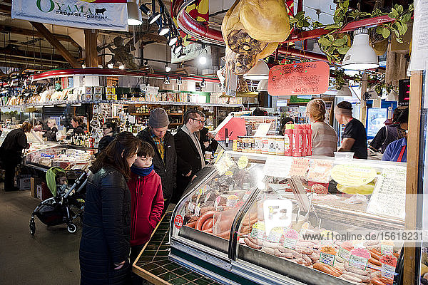 Customers look at meat in a deli case in a market on Granville Island  Vancouver  British Columbia.