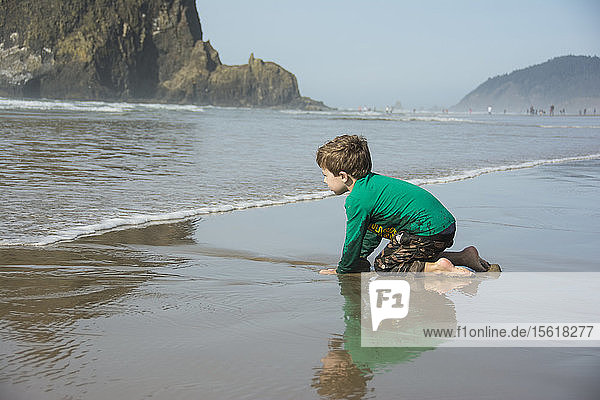 Ein kleiner Junge buddelt im Sand und freut sich auf die Wellen am Cannon Beach  Oregon.