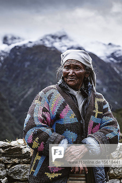 An elderly Sherpa woman standing in a colorful coat before the mountains on a ridge line near Namche Bazaar  Solu Khumbu  Nepal
